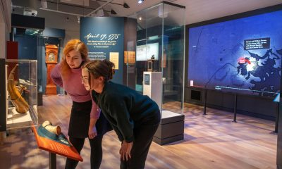 two visitors leaning into a display case in a gallery looking at a couple of pieces of scrimshaw.