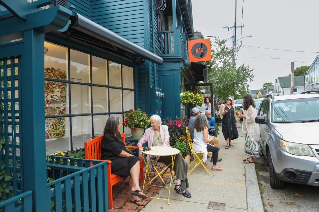 photo of a bustling street - people are sitting outside an art gallery while other are talking in groups in the background.