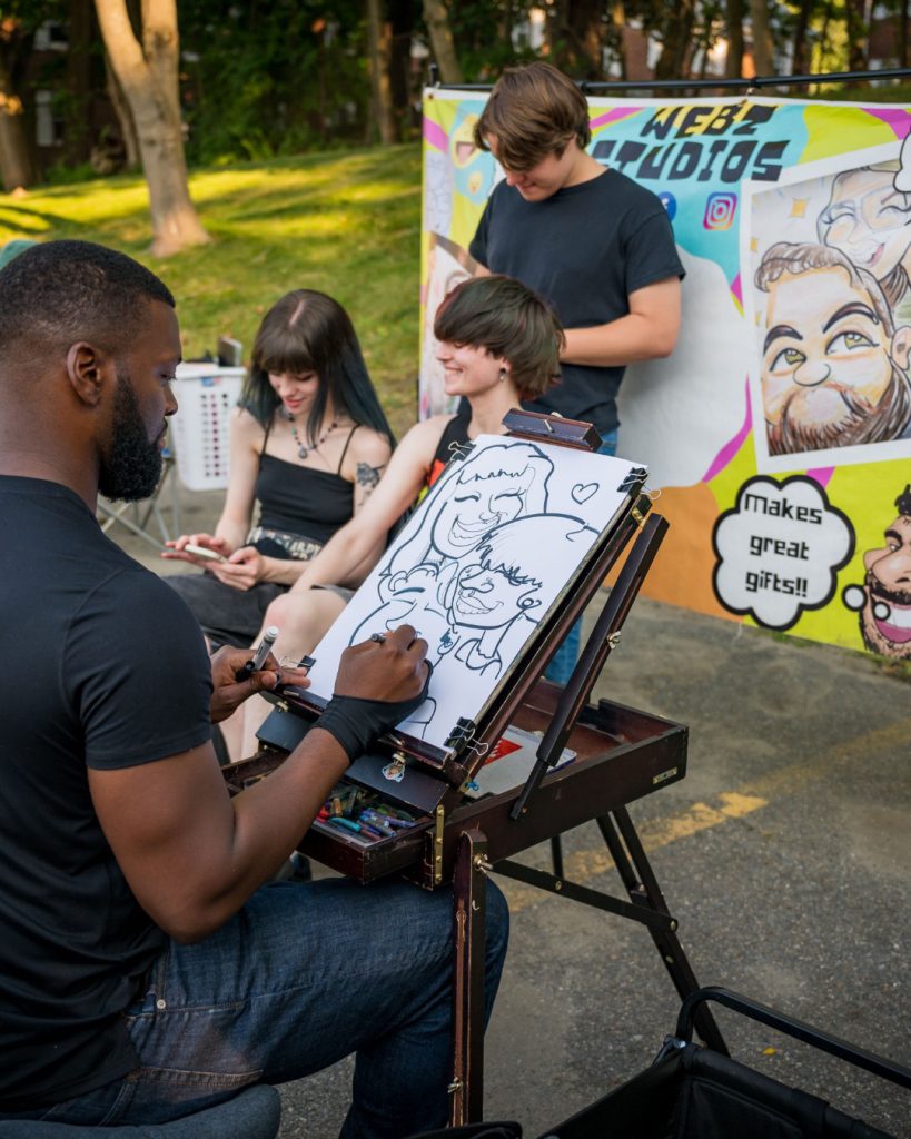 photo of a caricaturist drawing a couple at an outside festival.