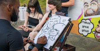 photo of a caricaturist drawing a couple at an outside festival.