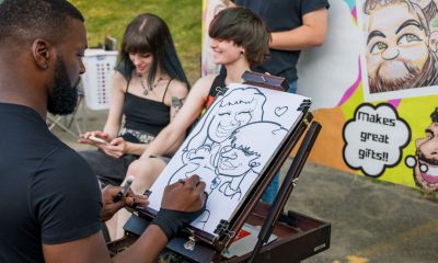 photo of a caricaturist drawing a couple at an outside festival.