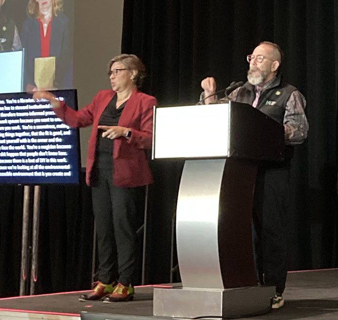 photo of a man and woman speaking at a podium.