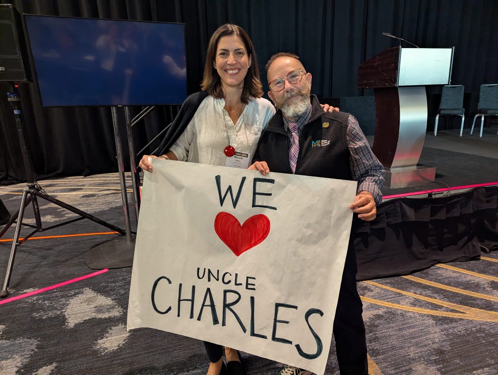 photo of a man and woman smiling together holding a large handmade poster that reads "We Heart Uncle Charles".
