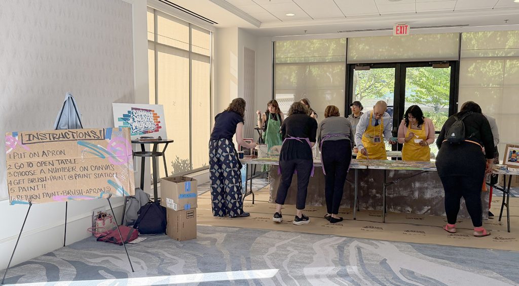 people bent over a long table painting on a shared canvas.