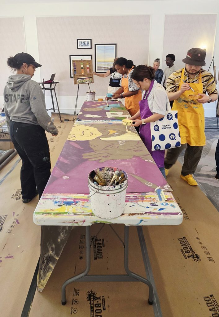 photo of people all contributing to a mural canvas propped up on a long table.