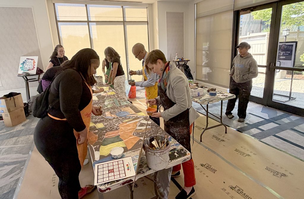 photo of people in aprons painting a long canvas.