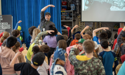 photo of a musician performing in front of a group of school children who are mirroring the way he's gesturing along with the song he's singing.