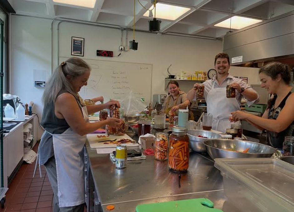 photo of a commercial kitchen with people wearing aprons and pickling carrots.