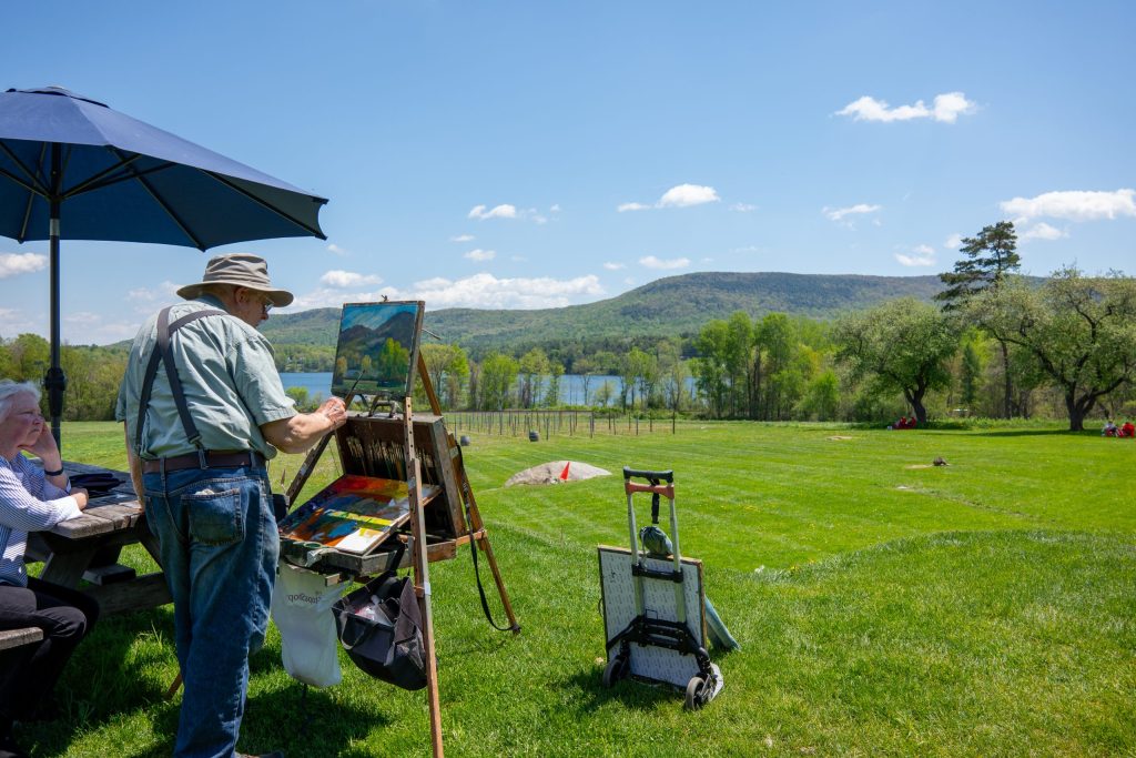 two elderly people painting on easels outside.