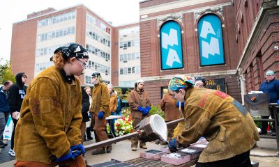 photo of 2 artists pouring liquid metal into molds outside at a public art making event.
