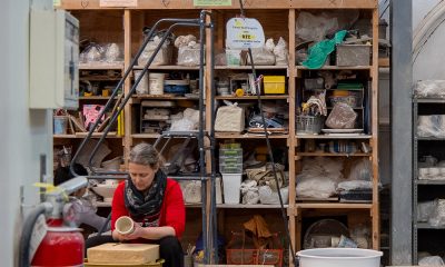 photo of a ceramics studio, a wall of supplies behind an artist working at the wheel.