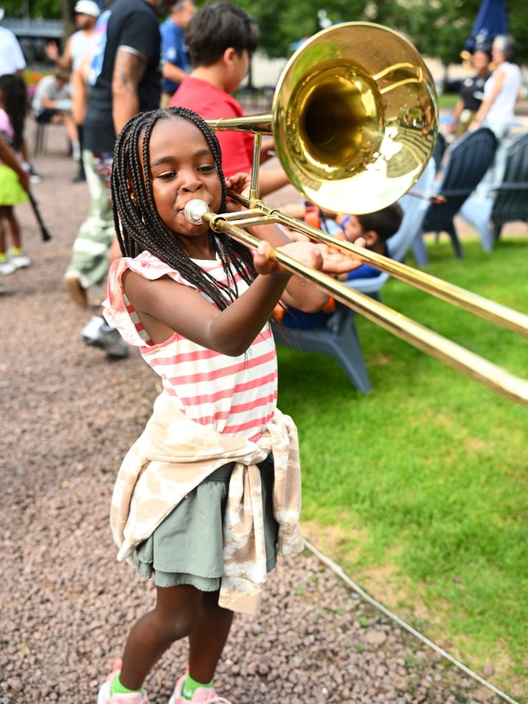 photo of a young girl playing a trombone that's longer than she is tall.