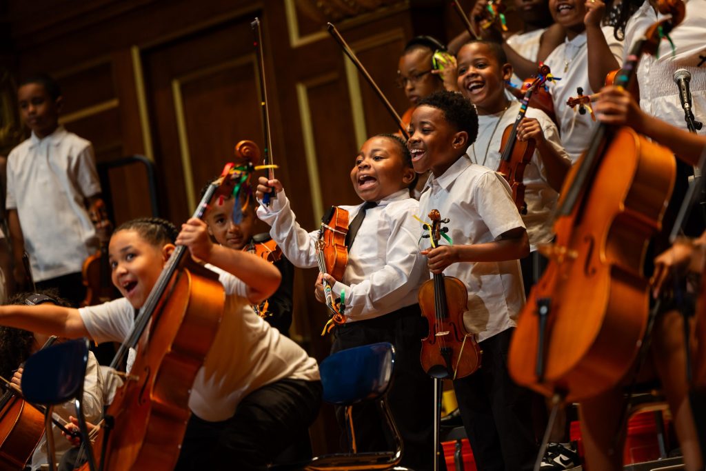 a group of young musicians laughing, holding their stringed instruments in between performing.