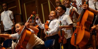a group of young musicians laughing, holding their stringed instruments in between performing.
