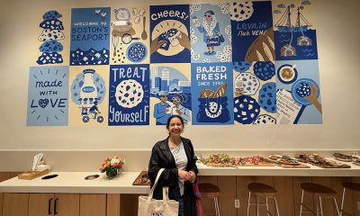 photo of the inside of a restaurant, a woman stands in front of a hand painted grid of images in various shades of blue.
