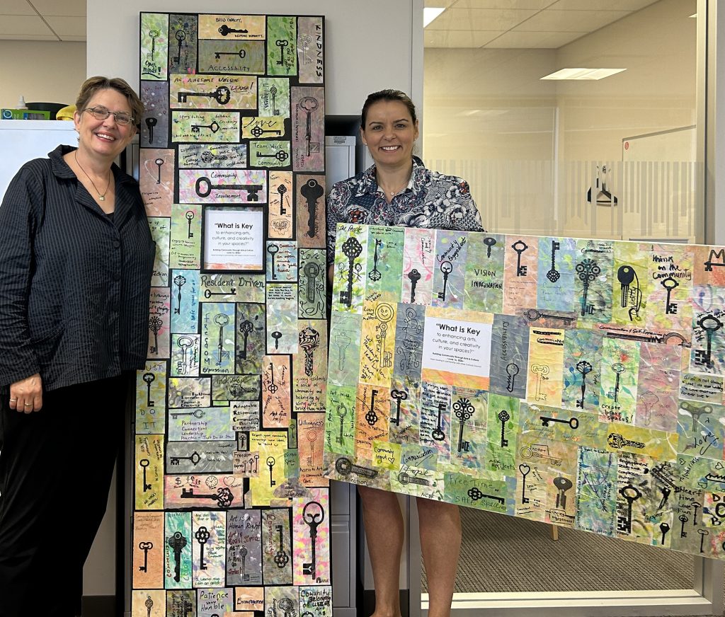photo of 2 women standing with two 6 foot long canvases making up the community art project described throughout this blog.