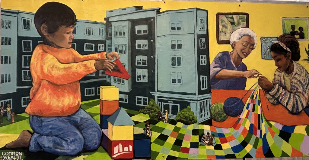 photo of a mural depicting a child building a tall structure out of blocks, tall housing developments in the background, and a grandmother and child sewing a garment that extends into the ground under which the child is building with blocks.